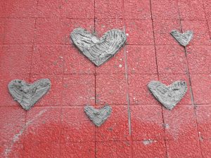 Foto van rode tegels, daarop cement in de vorm van hartjes.